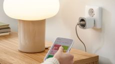 A hand holding a smartphone pointed towards the IKEA Inspelning smart plug