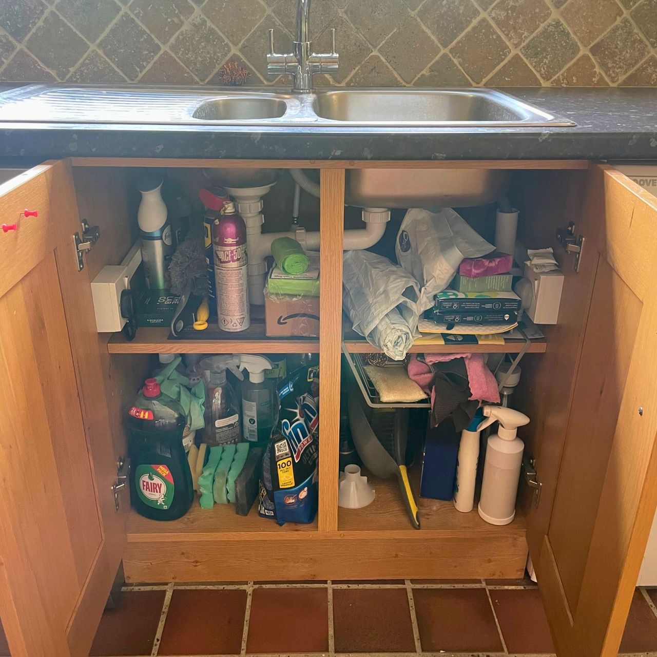 Messy under the sink cupboard filled with all kinds of cleaning products