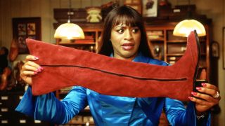 Chiwetel Ejiofor holding up a knee-high bright red boot in a wig and makeup in 2005's Kinky Boots