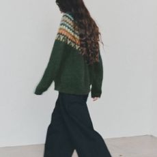 A female model wearing a dark green patterned jumper and black jeans from Toast.
