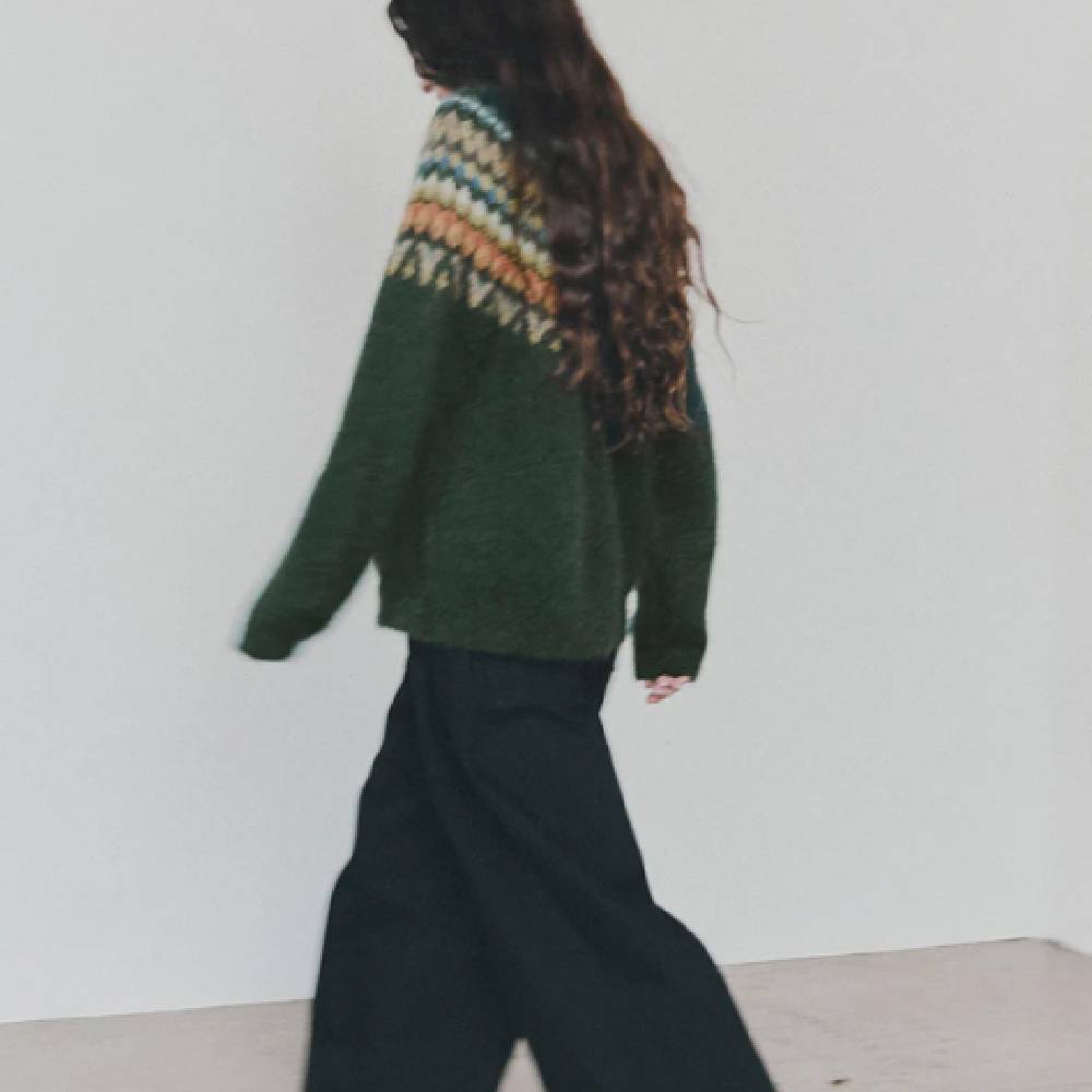 A female model wearing a dark green patterned jumper and black jeans from Toast.