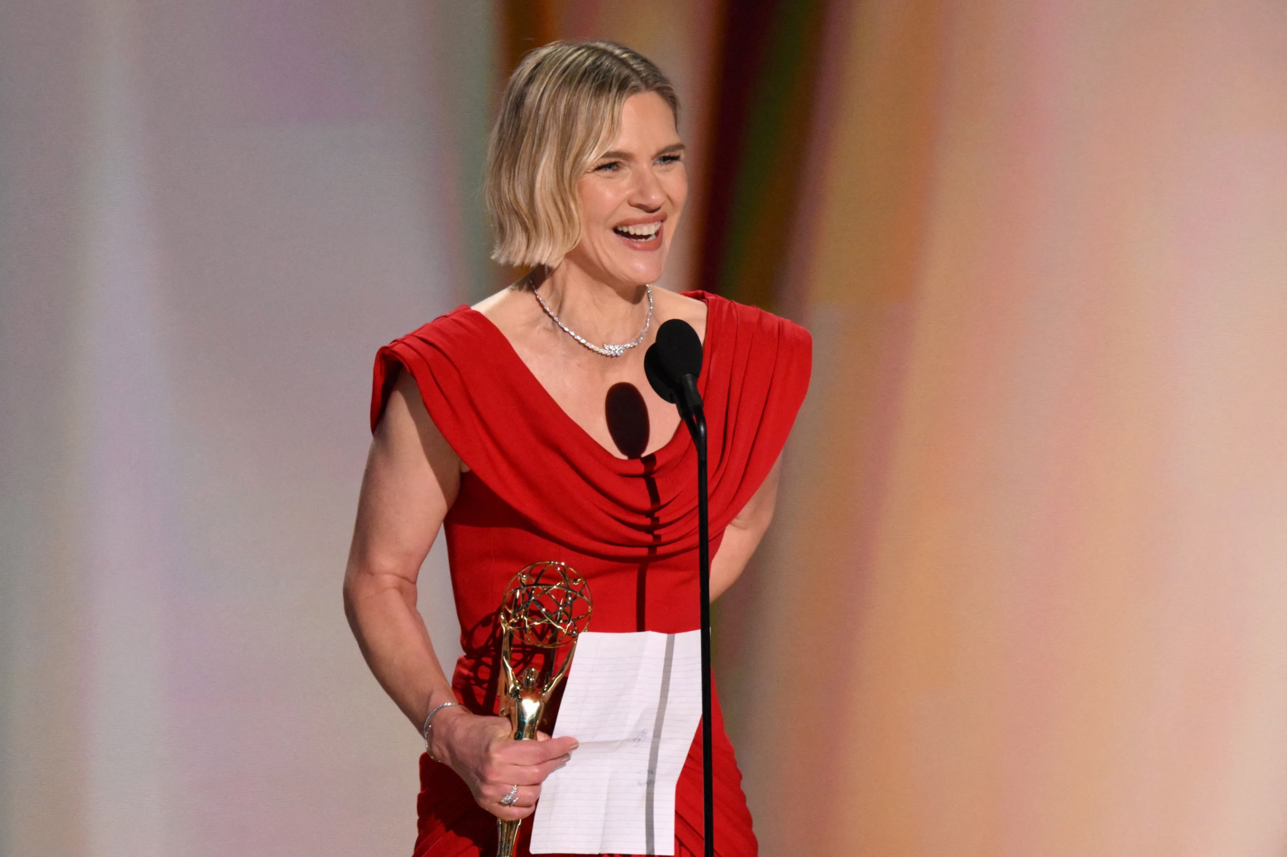 rhea seehorn wears a red dress and holds an emmy award and a speech as she smiles accepting the emmy for outstanding actress in a drama for pluribus at the 2026 awards