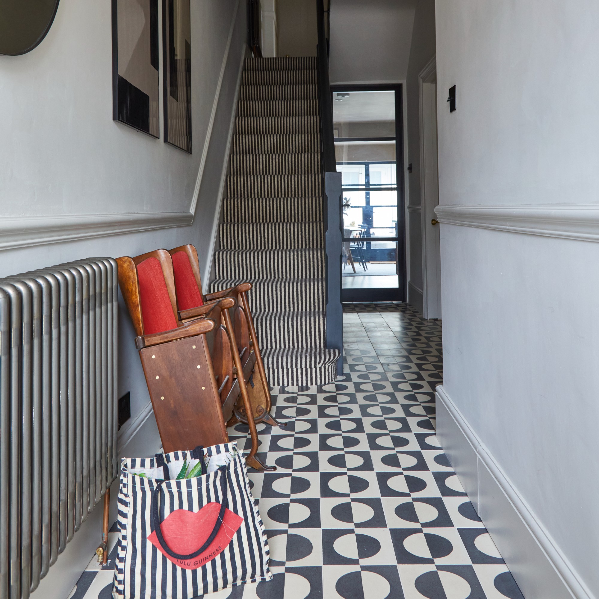 A grey, narrow hallway with a dado rail on the walls, graphic black and white tiled floor and a staircase