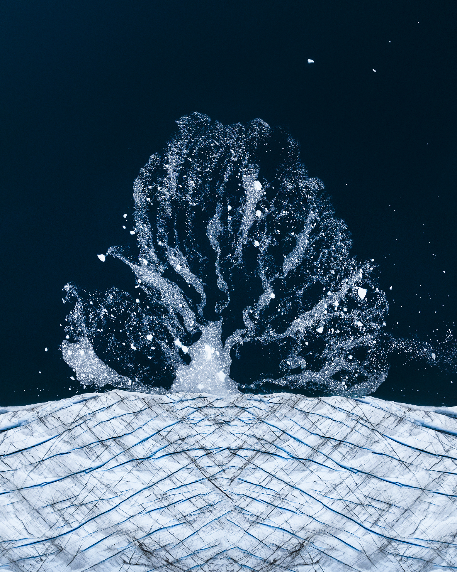 Aerial view of a dynamic splash emerging from icy waters, with intricate blue-veined ice patterns illuminated beneath