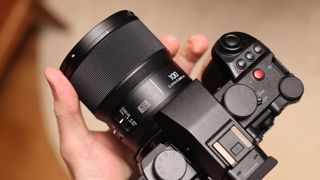 Panasonic Lumix S 100mm f/2.8 Macro lens attached to a Panasonic Lumic S5II and held in a hand