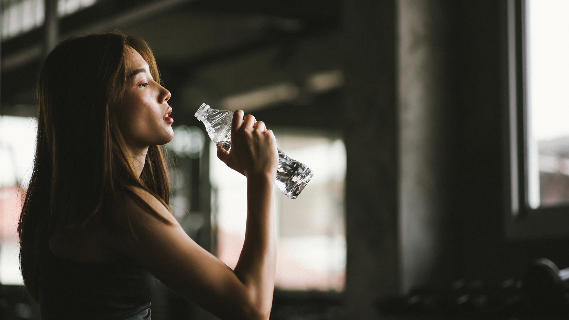 Side View Of Young Woman Drinking While Sitting In Gym - stock photo