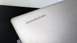 Close up of the Chromebook Plus badge on the lid of the Acer Chromebook Plus Enterprise 515, on a black desk against a white background.