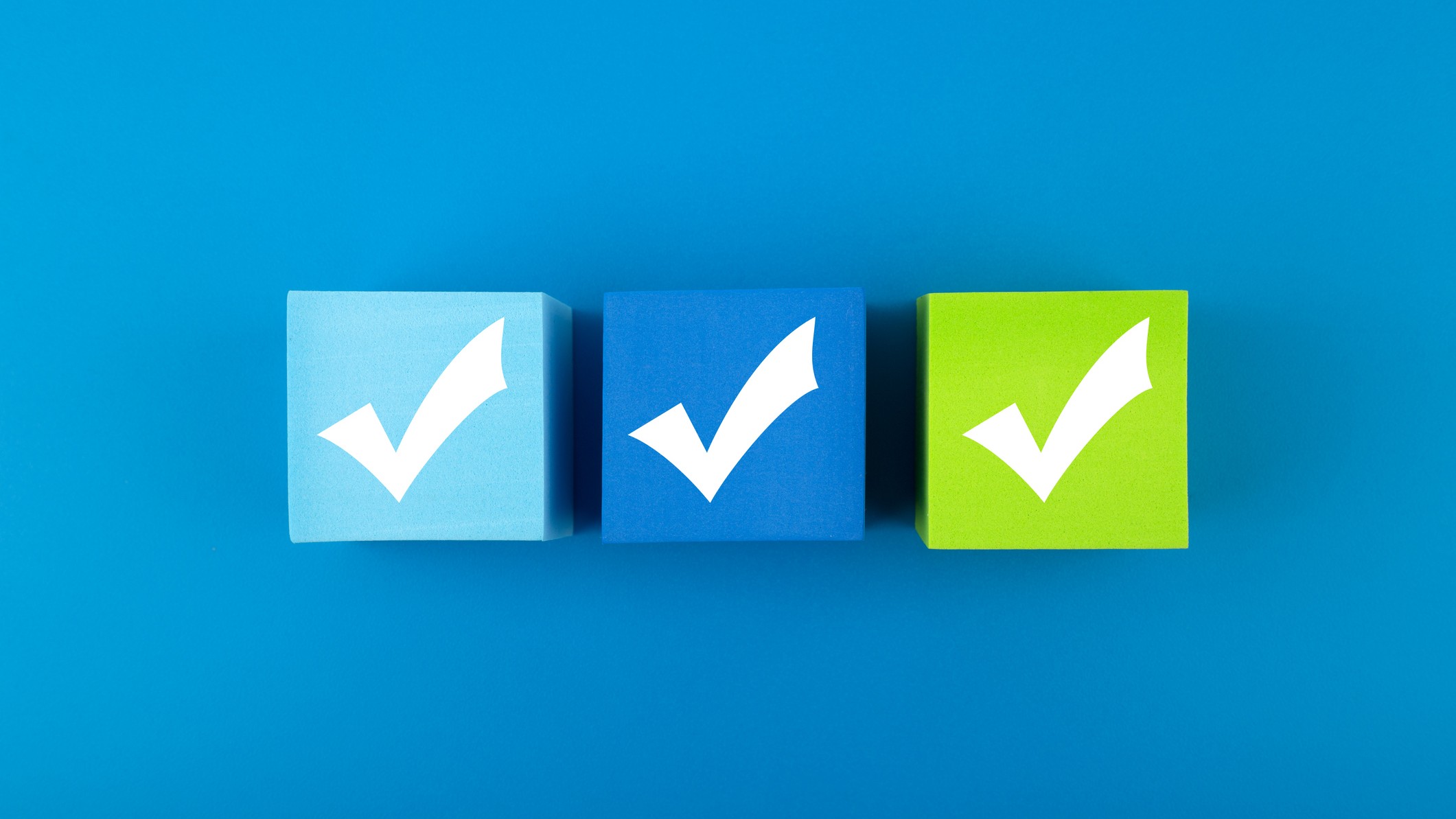 teal background with three wooden blocks in light blue, medium blue and green with checkmarks