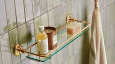 Gold and glass bathroom shelf with candles and toiletries on on pearly tiles