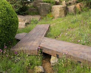 an oak boardwalk leading over a small stream and bog garden