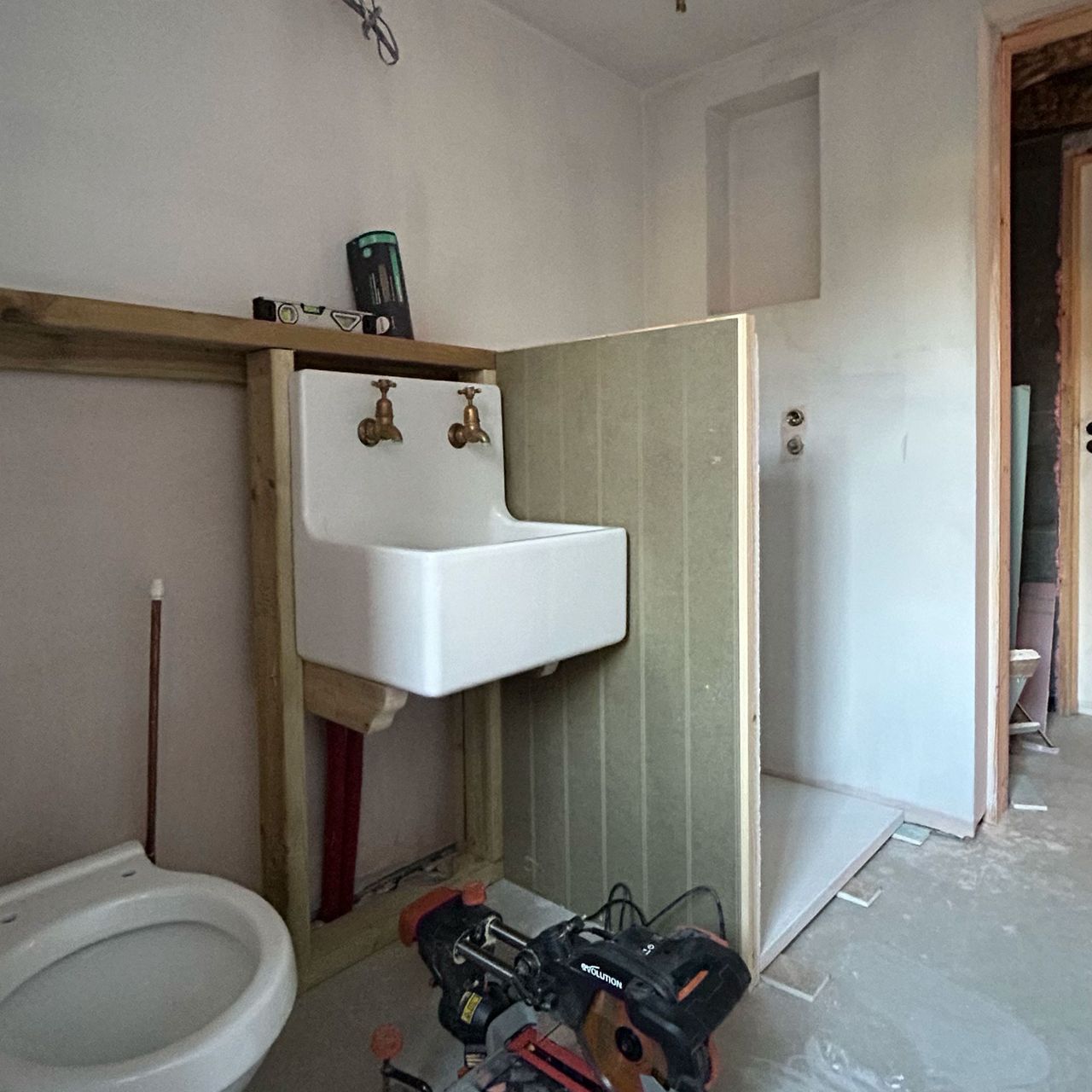 Bathroom mid-renovation with half-height stud wall erected between loo and sink and what will become shower enclosure