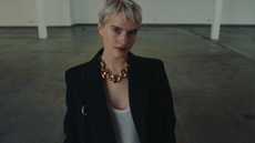 A woman with short blond hair wearing white top and black blazer, and a gold chain