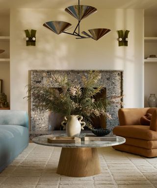 neutral living room with large marble fireplace and a blue velvet sofa with a caramel velvet armchair and large light fixture