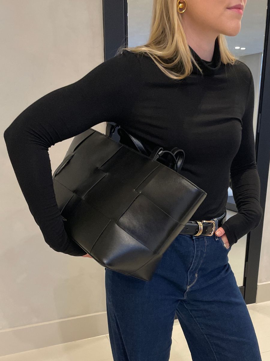 Woman wears black top, carries black leather bag