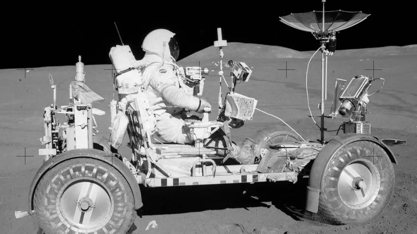 A black and white photo of an astronaut on a rover on the Moon. 