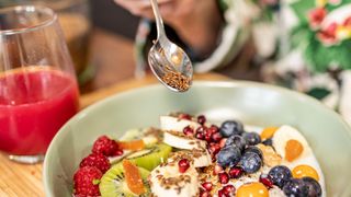 Spoon scattering flaxseeds onto bowl of oats and fruit