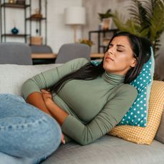 Feeling sick after a sex: A woman lying on the sofa clutching her stomach