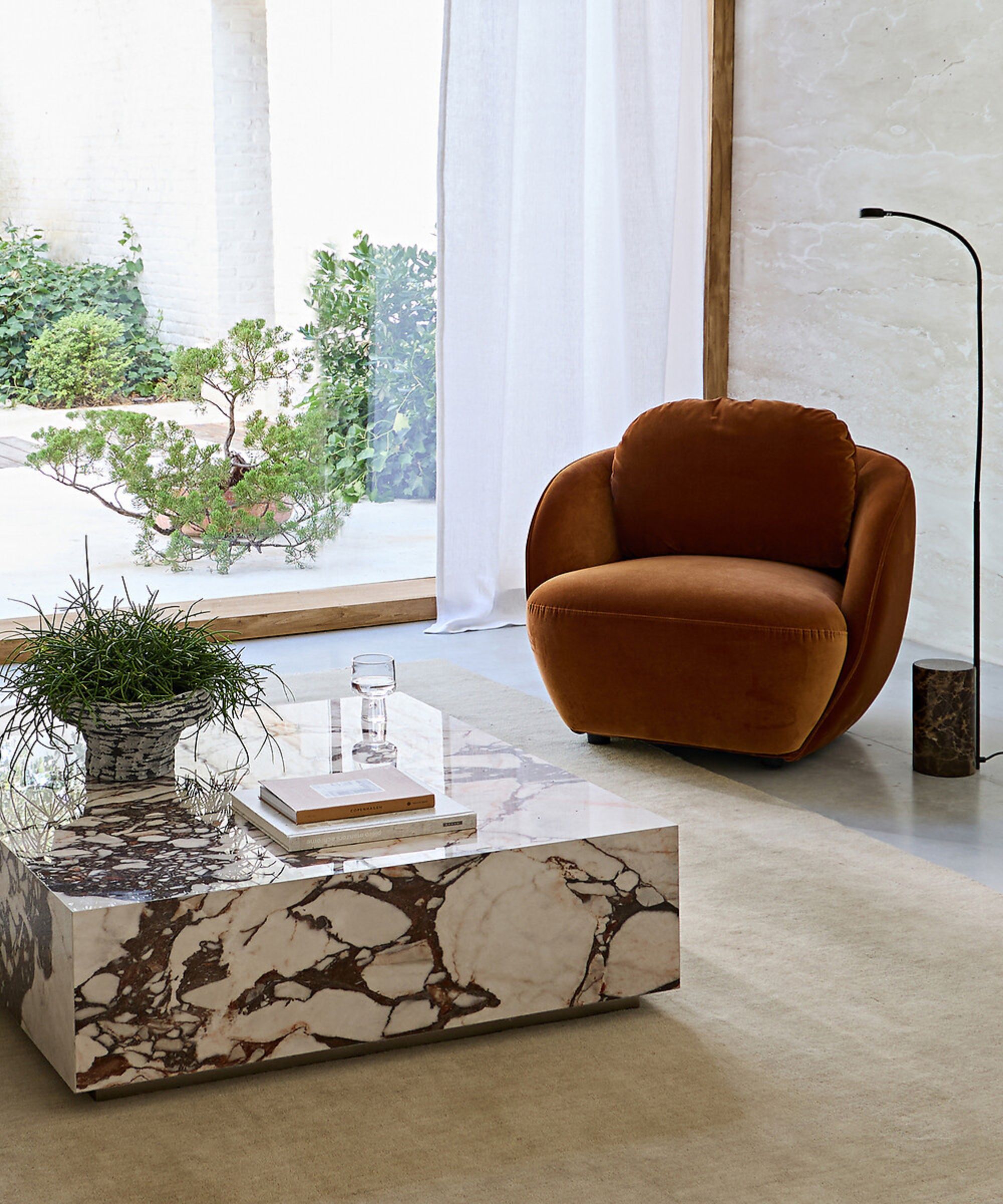 Living room dressed in La Redoute furniture including an orange velvet armchair, beige rug, marble square coffee table styled with books and a pot plant, and a floor lamp next to the chair