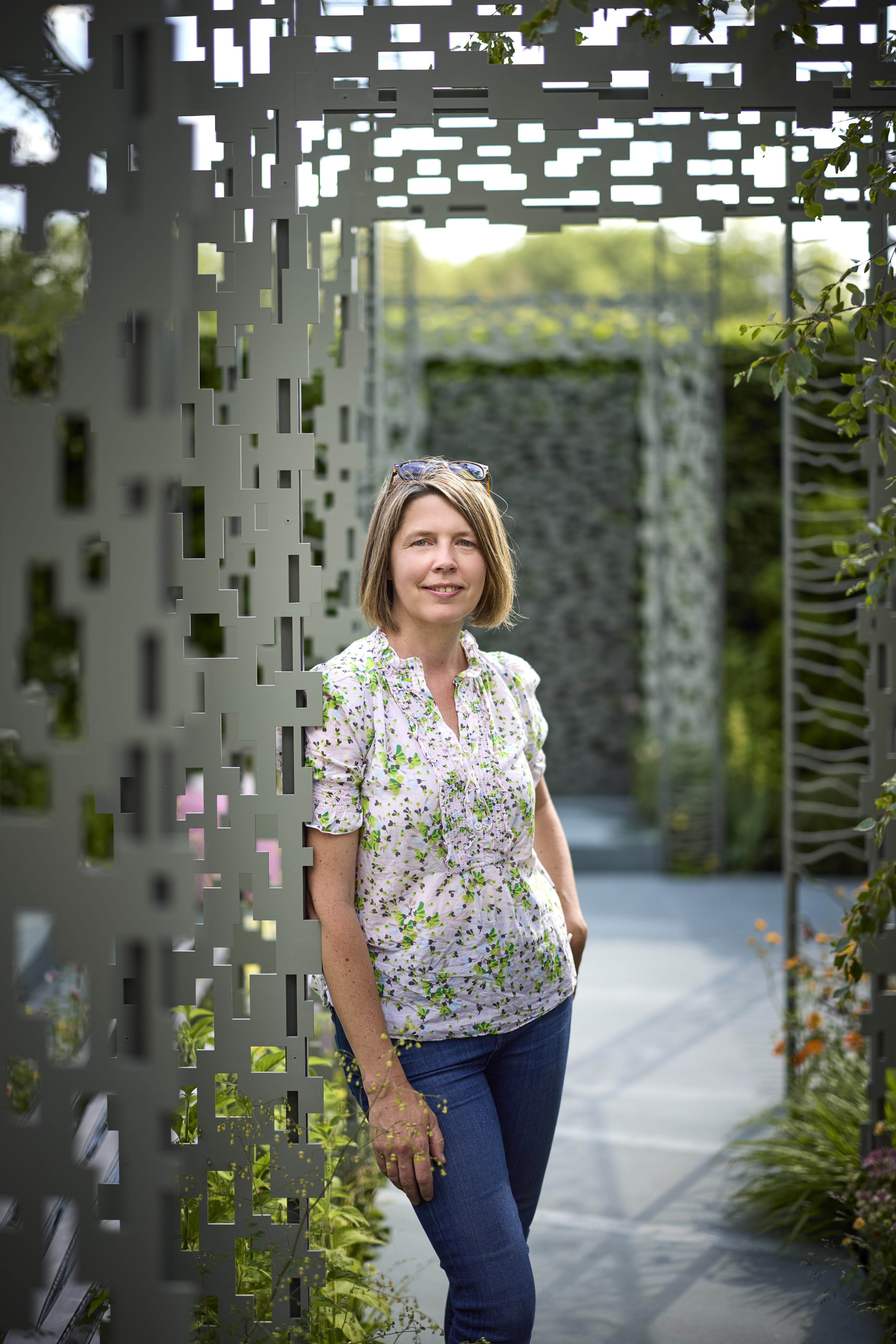 Female with short hair stands leaning against an arch in a garden at the RHS Chelsea Flower Show for Boodles.