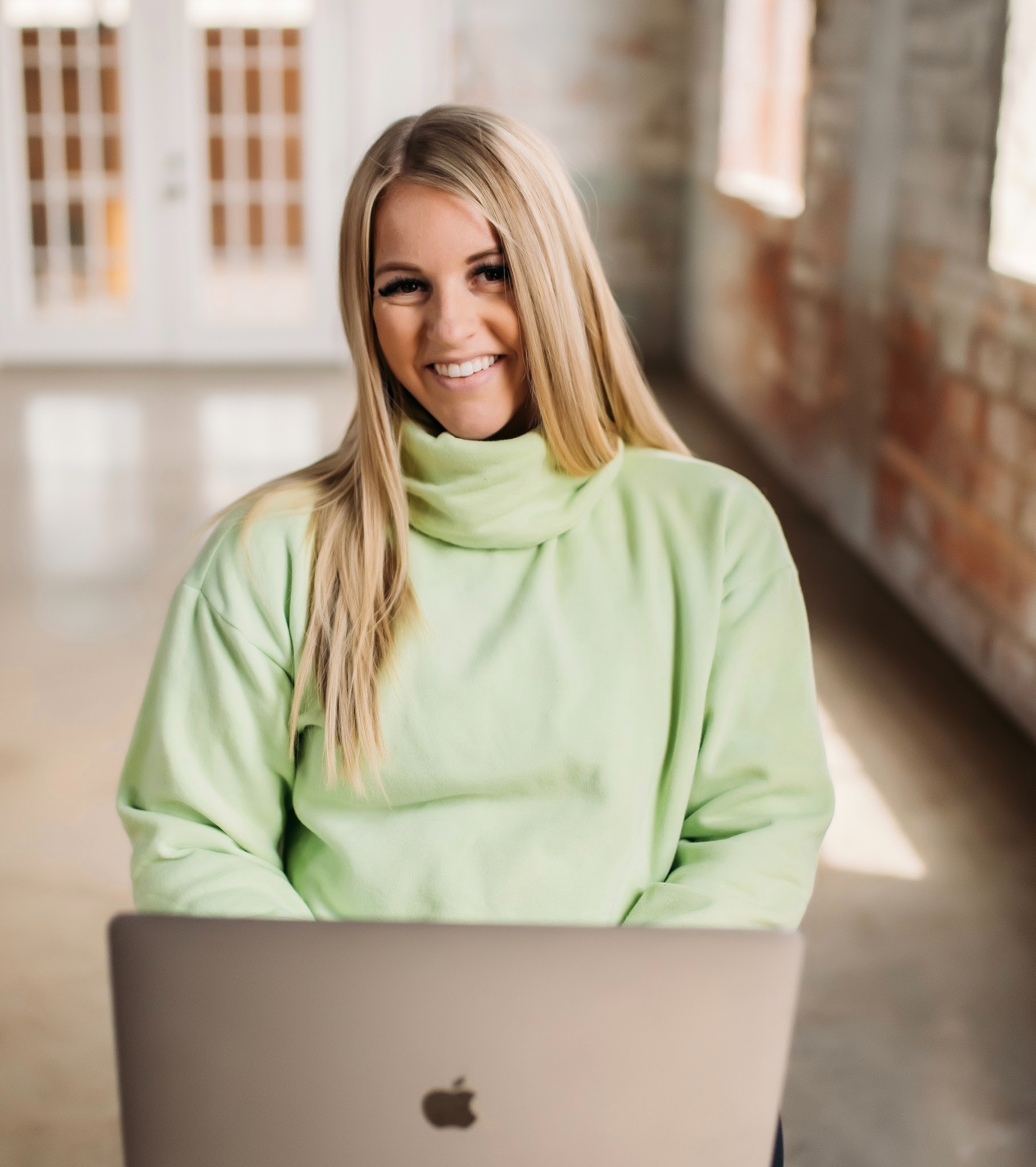 woman smiling at the camera waist up wearing a lime green top and an apple laptop in front of her