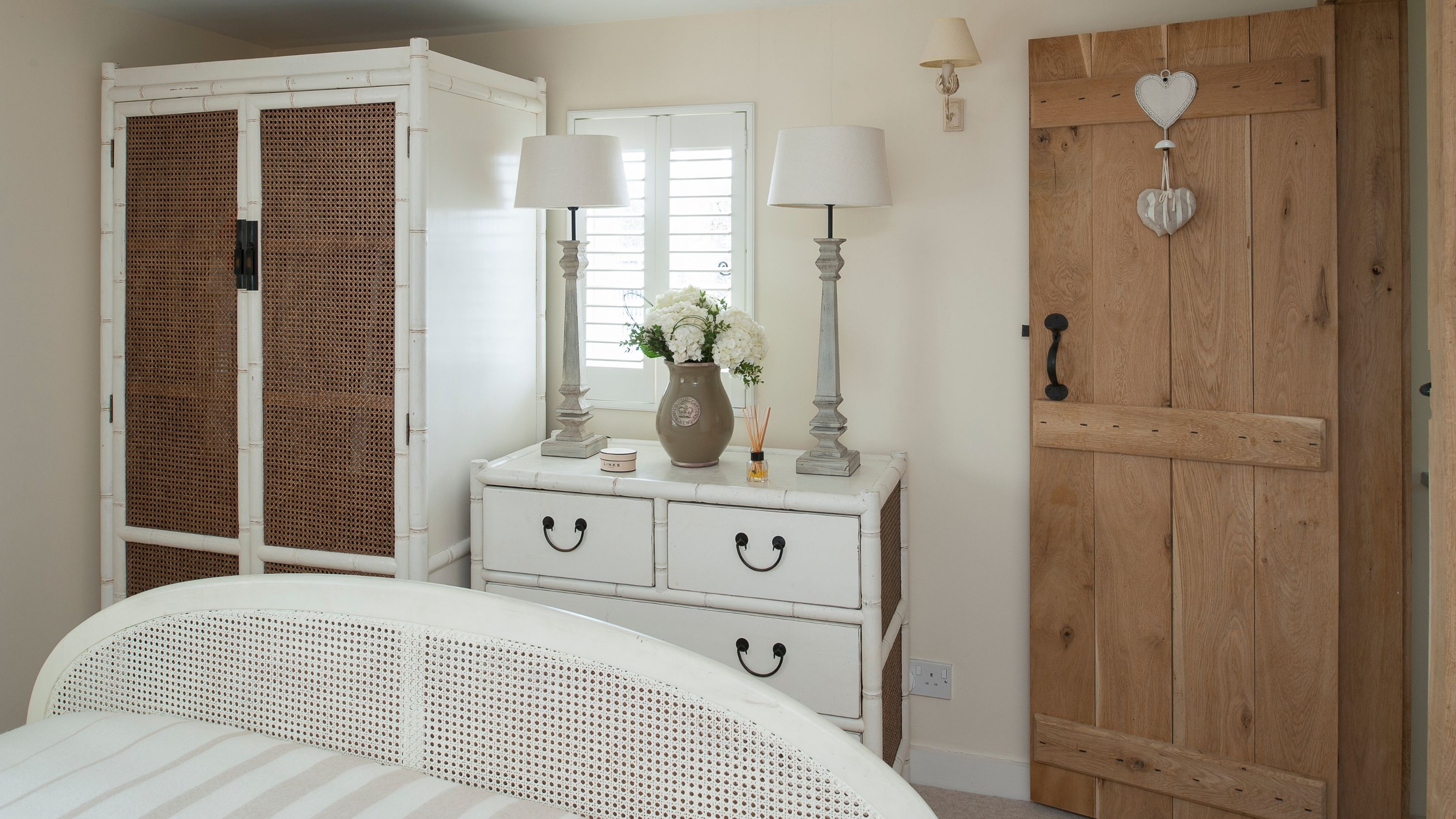 A cream bedroom with a wooden, cottage-style oak door and white, shabby chic bedroom furniture.