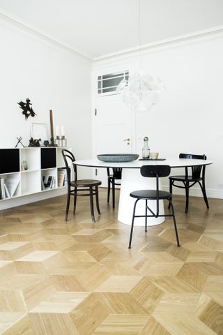 Dining room with table and chairs, wall hung strorage, white walls and parquet flooring