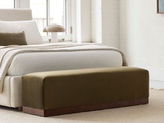 A khaki green bench by a bed