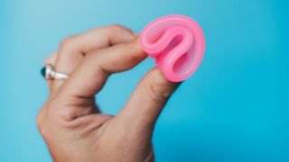 person holding pink menstrual cup on blue background