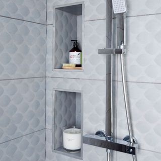 bathroom with grey tiles recessed shelves and shower