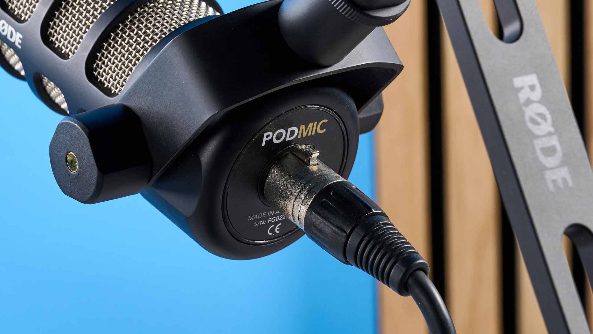the rode podmic podcast and broadcast microphone photographed with a blue background, shown with the rode ds2 desk stand