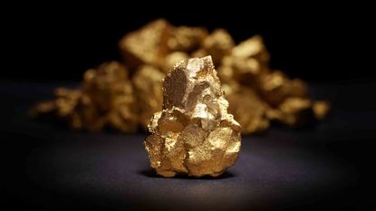 A picture of a large gold nugget in front of a lot of smaller gold nuggets