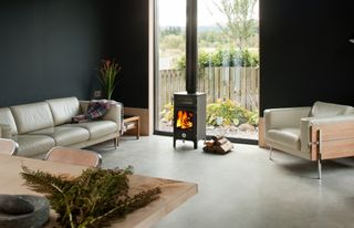 A living room with a roaring log burner, ply floors and black painted walls
