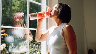 Woman drinking bottle water looking out of sunny window