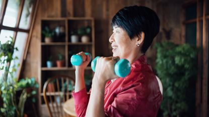 Woman holding light dumbbells by her shoulders. She is in a domestic setting.