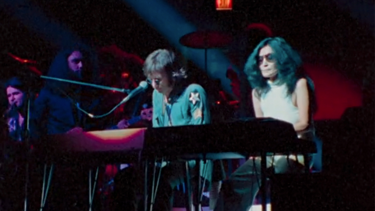John Lennon playing piano in concert with Yoko Ono sitting next to him.