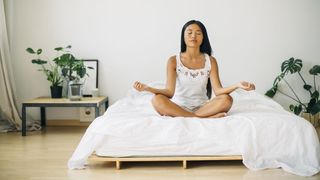 A woman sits on her white mattress practicing a breathing technique to help her fall asleep faster
