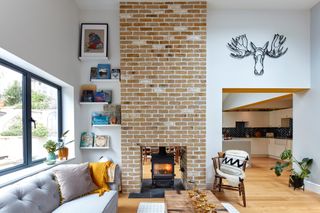 Living room with white walls, grey sofa, open shelving for books, and brick chimney with woodburning stove