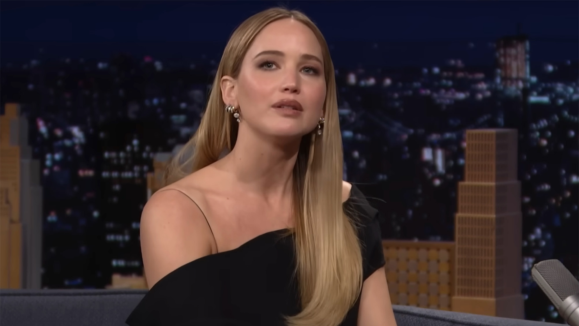 Jennifer Lawrence rocks a black top and dangly earrings while sitting in a chair on the Tonight Show Starring Jimmy Fallon. 