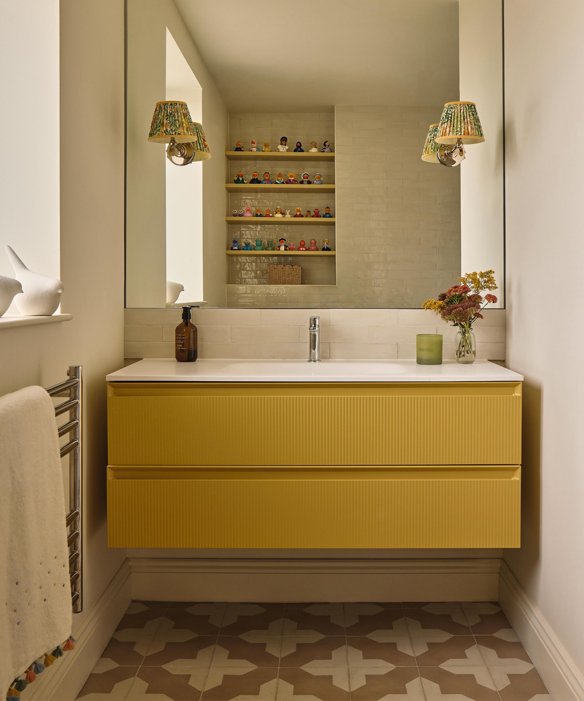 a small bathroom vanity area with a floating fluted vanity painted bright yellow with patterned floor tiles
