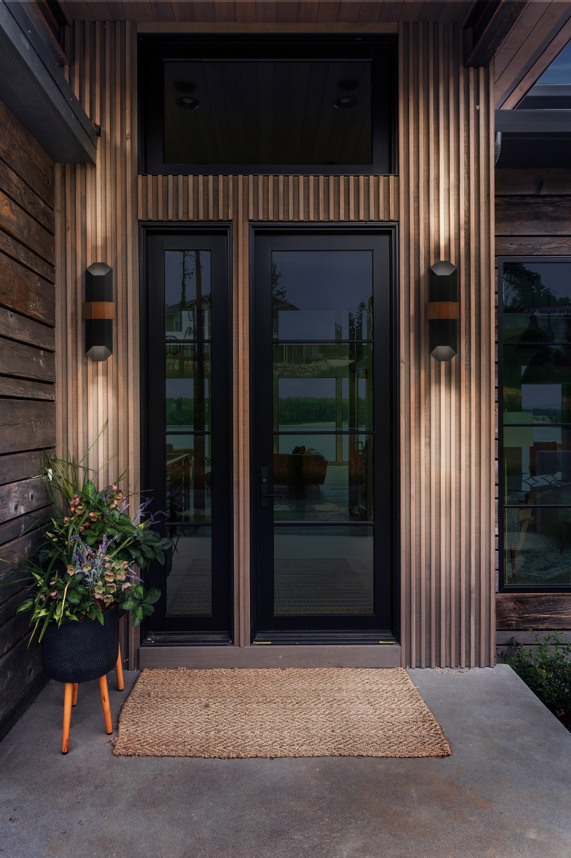 The exterior of a modern property with glass doors, a woven doormat, and two contemporary up/down lights flanking the door