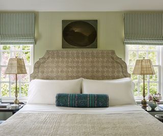 Upholstered headboard with stripe blinds, neutral bedside lamps and blue bolster cushion