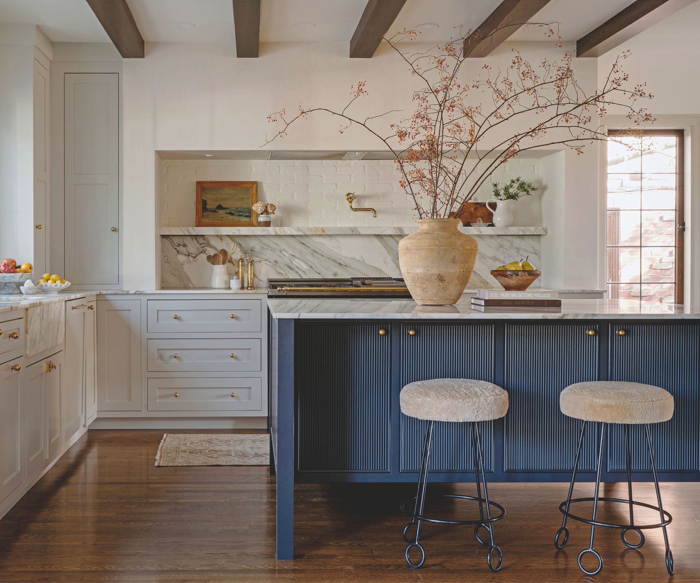 cream kitchen with blue fluted island and cream bar stools with large terracotta vase filled with stems