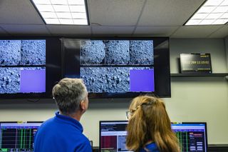 Two NASA researchers watch a wall of screens showing the rocky surface of the asteroid Dimorphos, moments before the DART spacecraft smashes into it