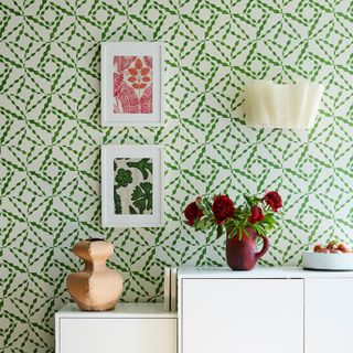 Cream wall light on green and white patterned wallpaper with artwork