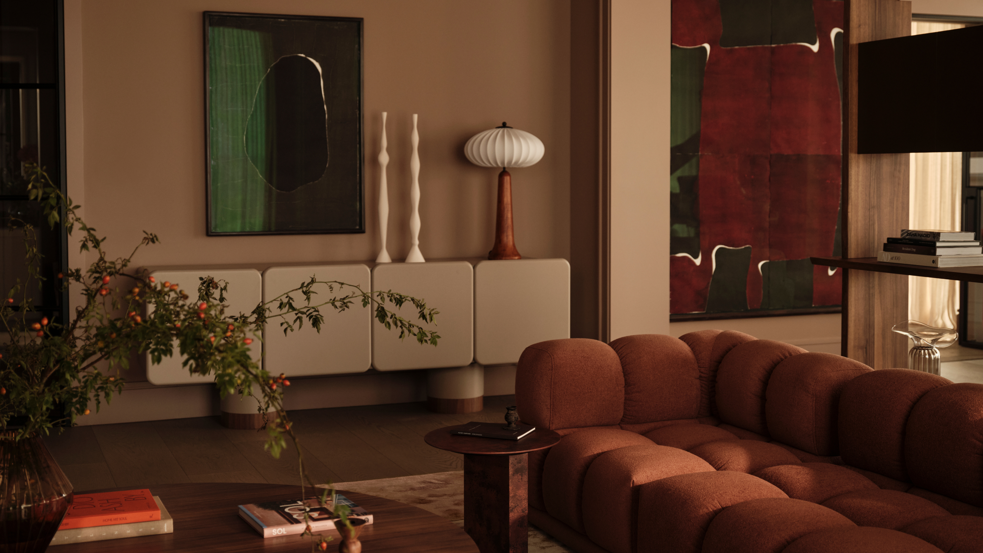 A modern living room with a contemporary rust sofa, earth tones, decorative accessories and artwork and a vase of foliage with berries on the round coffee table