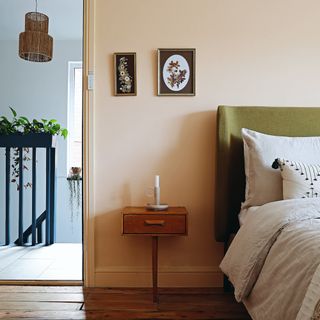 Light orange painted bedroom, green headboard, neutral bedding, wooden bedside table