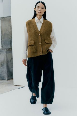 A model wearing a Cordera outfit of black pants, a button-down shirt, and a green cardigan