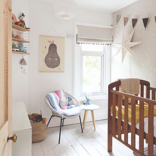 Wooden cot in neutral white and grey nursery with arm chair and coloured cushion plus wall art