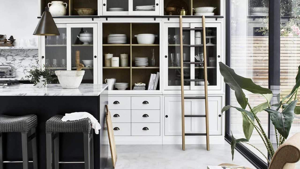 A monochrome kitchen with black island, white dresser and wooden ladder