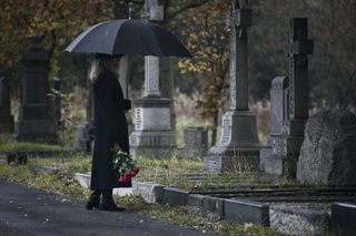 A widow brings roses to a grave on a rainy day.